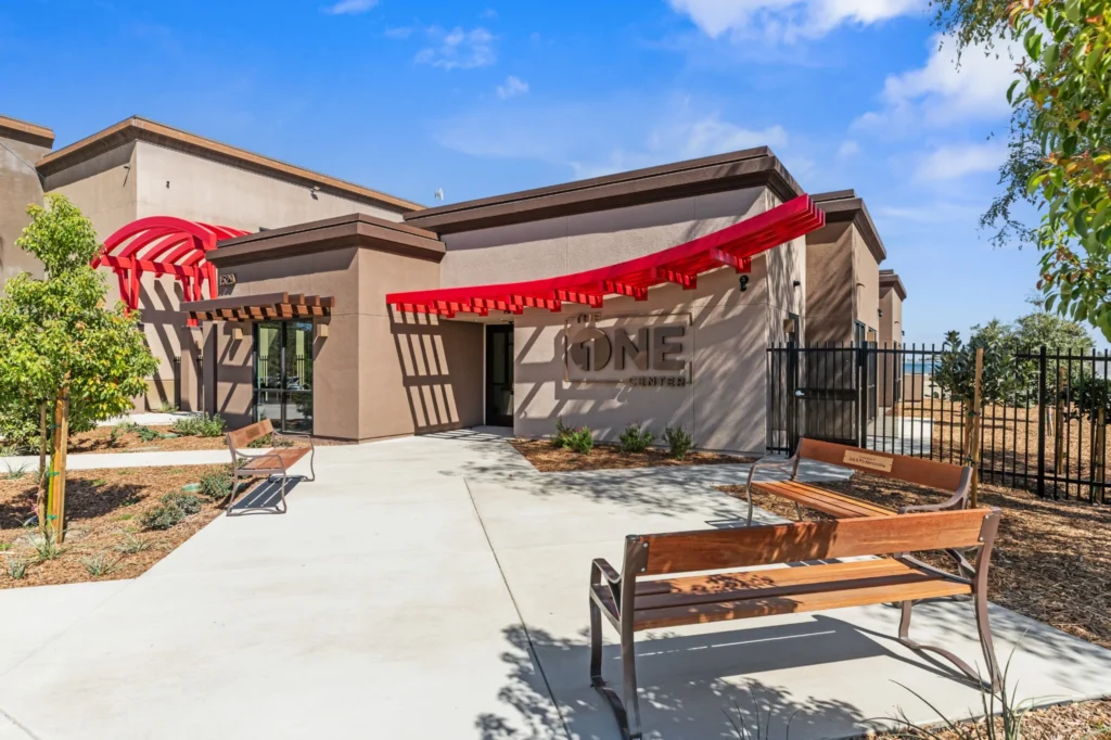Front entrance to Crossroads Grace Community Church’s counseling building, with red shade canopies, concrete walkways, landscaping, and benches.